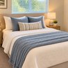 Bedroom with upholstered headboard, blue and cream bedding, and nightstand lamps